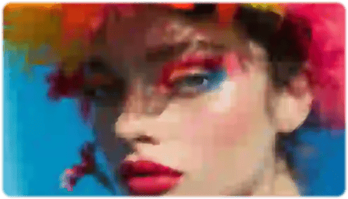 Foto sfocata di una donna con ombretto blu e arancione, rossetto rosso e un copricapo di piume multicolore.
