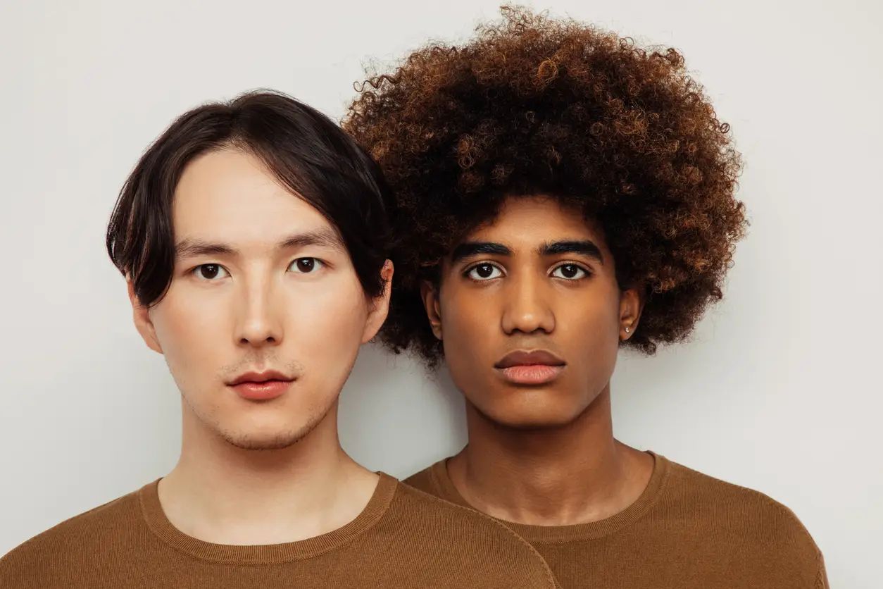 Zwei Männer, ein Asiate und ein Afroamerikaner, präsentieren zwei unterschiedliche KI-Frisuren.