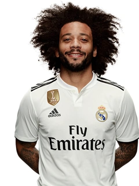 Retrato de Marcelo Vieira com grande afro preto e barba, vestindo camisa branca do Real Madrid, sobre fundo branco liso, sorrindo para a câmera.