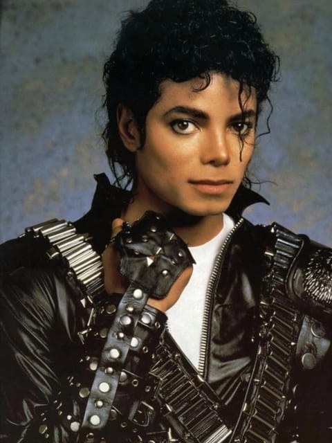 Retrato de estúdio de Michael Jackson com seu cabelo preto encaracolado e volumoso característico. Ele veste uma jaqueta de couro preta adornada com tachas prateadas e alças metálicas, uma camiseta branca com gola redonda e o fundo é um gradiente suave de tons de azul claro e amarelo claro. Modelo para troca de rosto de imagem.