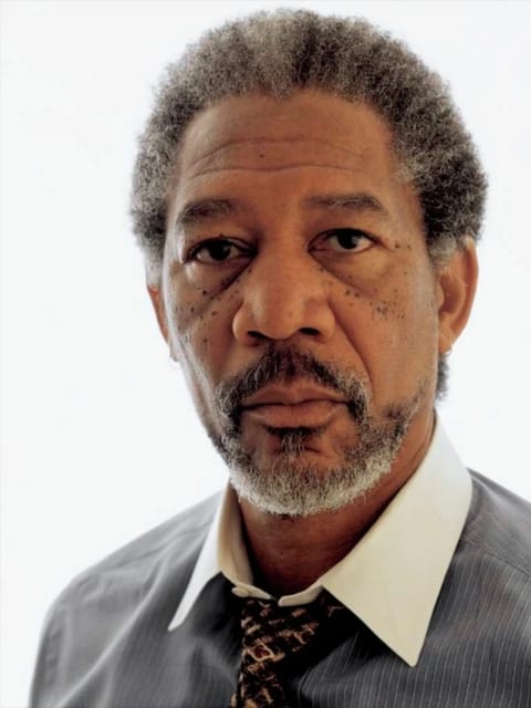 Retrato de Morgan Freeman com cabelo curto e grisalho com textura afro grisalha. Ele veste uma camisa listrada cinza claro com gola branca e gravata escura estampada, contra um fundo branco liso com um olhar calmo e direto para a câmera. Modelo para troca de rosto de imagem.