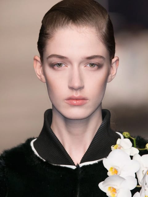 Retrato de uma modelo com cabelo liso puxado para trás andando na passarela, vestindo uma roupa preta adornada com orquídea branca. Modelo para troca de rosto de imagem.