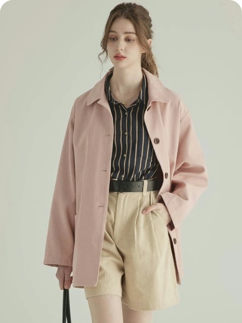Una mujer con una chaqueta rosa, camisa a rayas y pantalones cortos beige, sosteniendo un bolso beige, con botas marrones, modelo para el intercambio de ropa de AI.