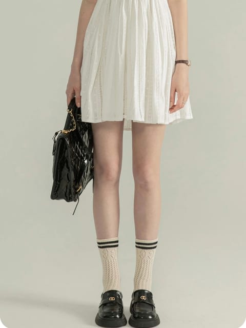 Una mujer con un vestido blanco sin mangas, sosteniendo un bolso negro, con zapatos negros y calcetines estampados, modelo para el intercambio de ropa de AI.