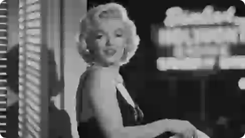 Foto hitam putih Marilyn Monroe mengenakan gaun hitam dan kalung mutiara.