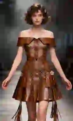 Portrait of a woman with short brown curls wearing a brown off-the-shoulder A-line pleated leather dress with a lapel collar, walking on a runway with a smoky backdrop. Template for an image-to-image tool.