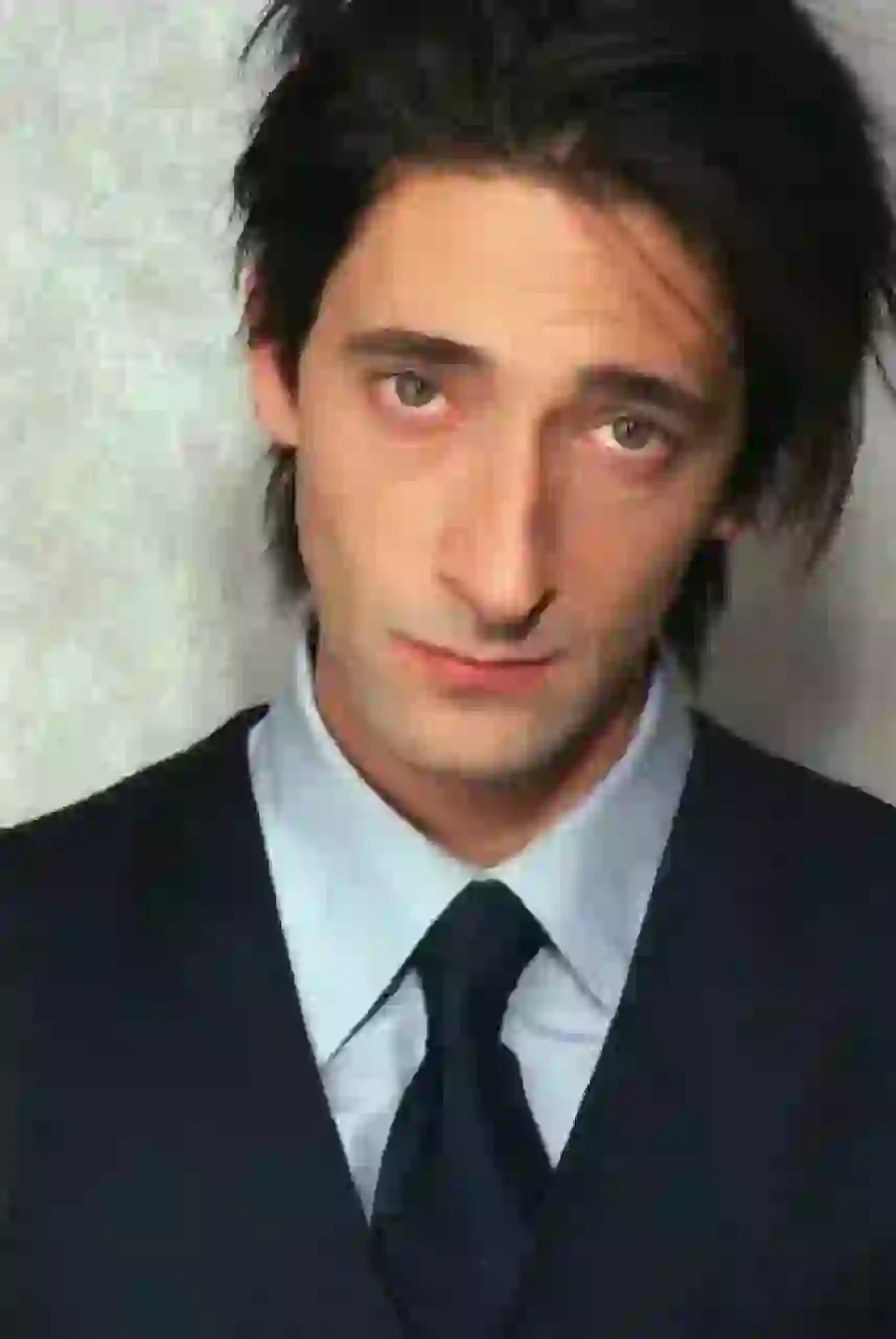 Porträtt av Adrien Brody med stökigt texturerat svart hår. Han bär svart kostym tillsammans med ljusblå skjorta och svart slips. Mall för bildbyte av ansikte.