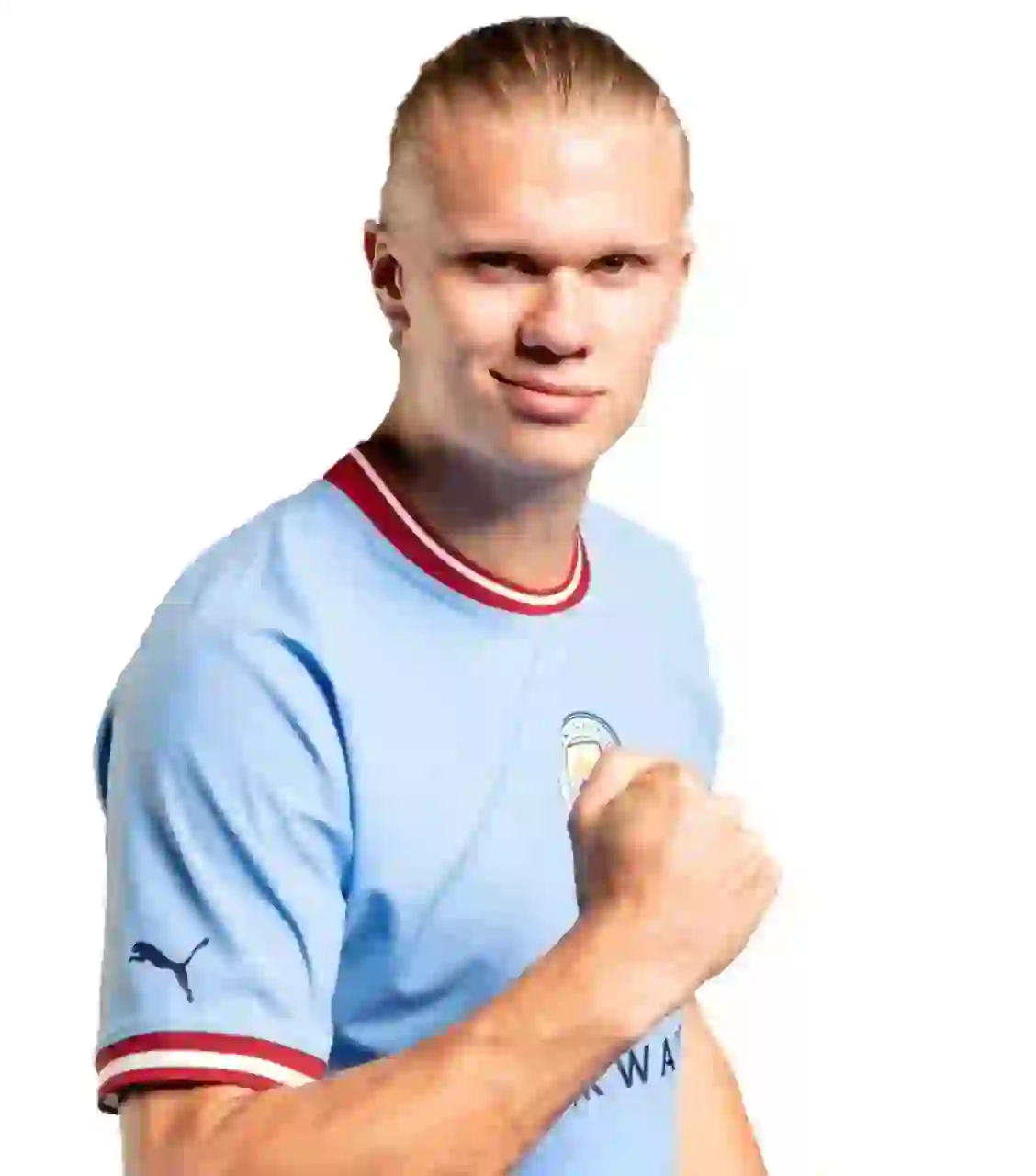 Porträtt av Erling Haaland med blont hår med slank bakåt, iklädd Manchester Citys ljusblå hemmatröja med röd-vit krage. Han har en näve upphöjd och ett lätt leende mot en vanlig vit bakgrund.