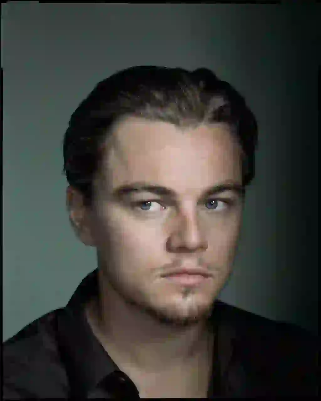 Porträtt av Leonardo Dicaprio med slank rygg i svart skjorta, poserar i en studio med en mörk belysning med grön bakgrund och tittar utanför kameran med ett lugnt uttryck. Mall för bildbyte av ansikte.