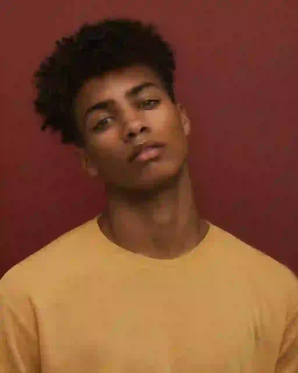 Porträtt av en man med svart afro och lugnt uttryck, klädd i en gul topp med rund hals, luta huvudet åt sidan. Mall för bildbyte av ansikte.