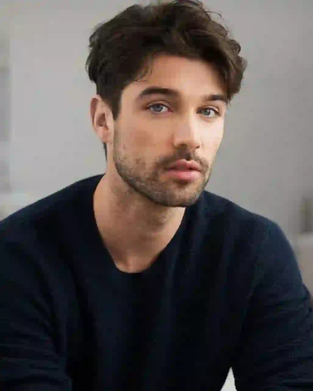 Portrait d'un homme aux cheveux brun foncé épais et ondulés, coiffés dans un look texturé en désordre, dans un pull bleu marine, assis dans une scène d'intérieur avec une expression calme. Modèle pour l'échange de visage d'image.
