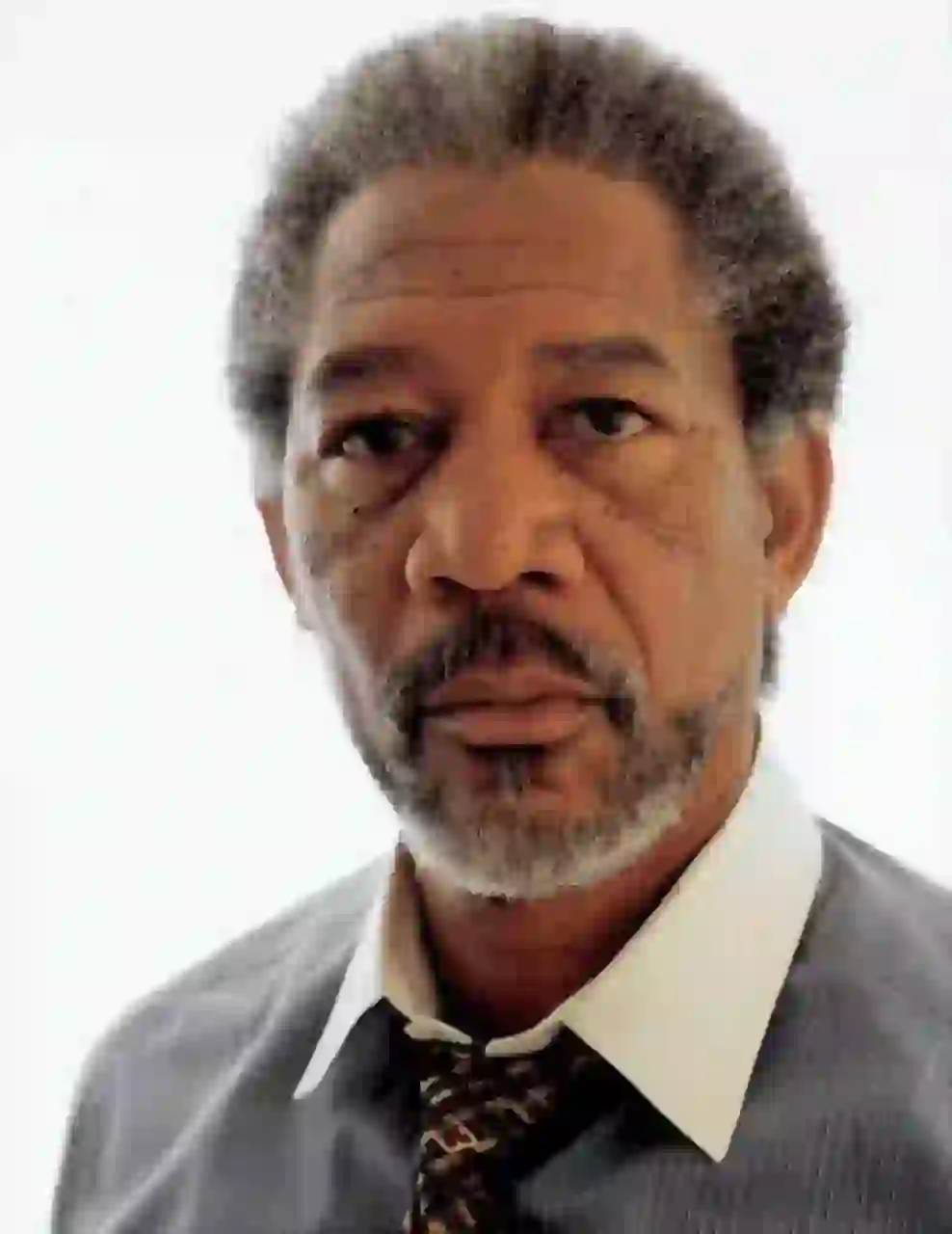 Porträtt av Morgan Freeman med kort grått salt-och-peppar afro-texturerat hår. Han bär en ljusgrå kritrandig skjorta med en skarp vit krage och mönstrad mörk slips, mot en vanlig vit bakgrund med en lugn, direkt blick mot kameran. Mall för bildbyte av ansikte.