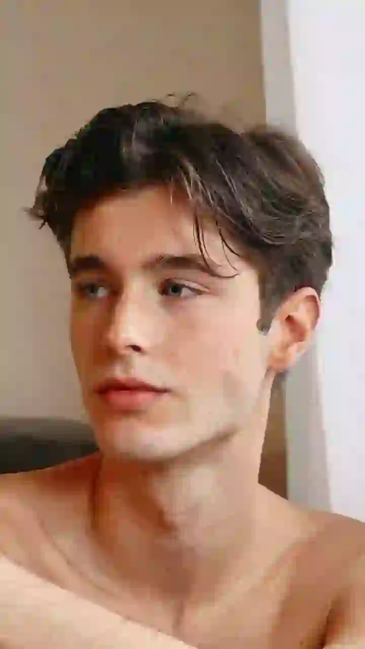 Porträtt av en man utan bar överkropp med tjockt vågigt brunt hår som sitter i en inomhusscen och tittar utanför kameran med ett lugnt uttryck. Mall för bildbyte av ansikte.