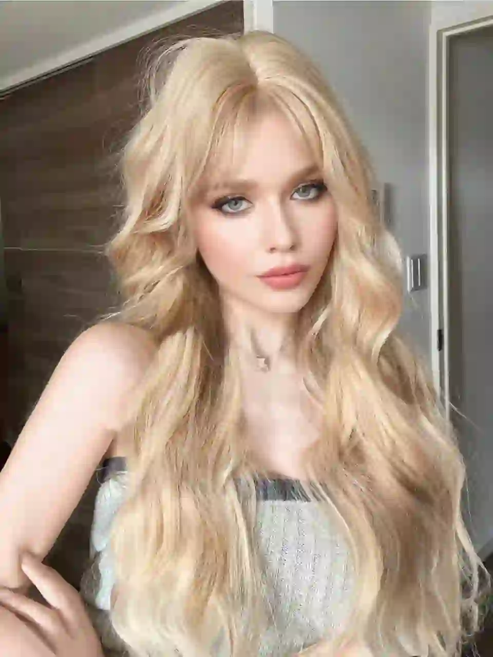 Portrait d'une femme aux cheveux blonds ondulés en débardeur tricoté gris sans bretelles, posant dans une scène d'intérieur. Modèle pour l'échange de visage d'image.