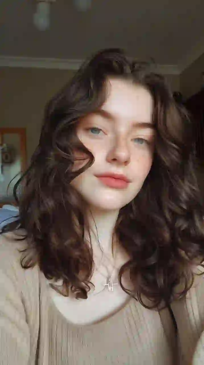 Selfie d'une femme aux cheveux bruns bouclés en haut kaki, souriant à la caméra. Modèle pour l'échange de visage d'image.