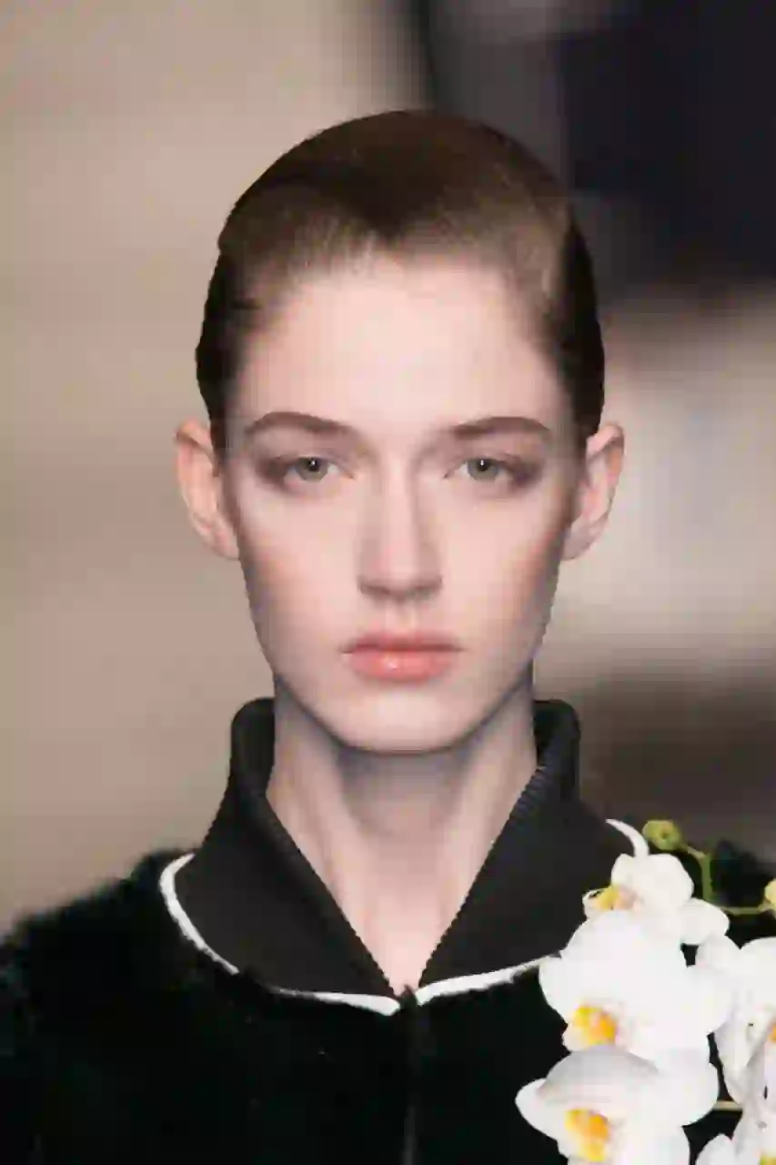 Portrait d'un mannequin aux cheveux lisses tirés en arrière défilant sur le podium, vêtu d'une tenue noire ornée d'une orchidée blanche. Modèle pour l'échange de visage d'image.