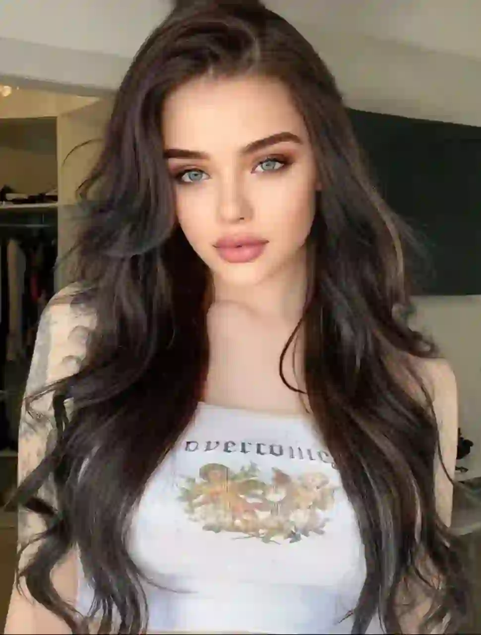 Selfie d'une femme aux cheveux noirs ondulés portant un débardeur blanc à motif Cupidon, posant à l'intérieur. Modèle pour l'échange de visage d'image.