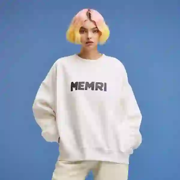 Pembe ve sarı saçlı, beyaz sweatshirt ve beyaz pantolonlu kadın kameraya poz veriyor.