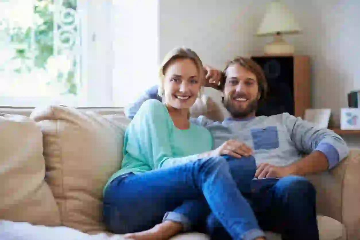 This is a couple in a commercial, hugging each other while sitting on their couch at home. This is how they look before the video face swap.