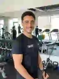 Hình ảnh do AI tạo ra về một huấn luyện viên thể hình mặc áo sơ mi đen đang tập luyện với thiết bị cáp trong phòng tập thể dục có ánh sáng tốt. Mẫu cho trình tạo ký tự South Park.