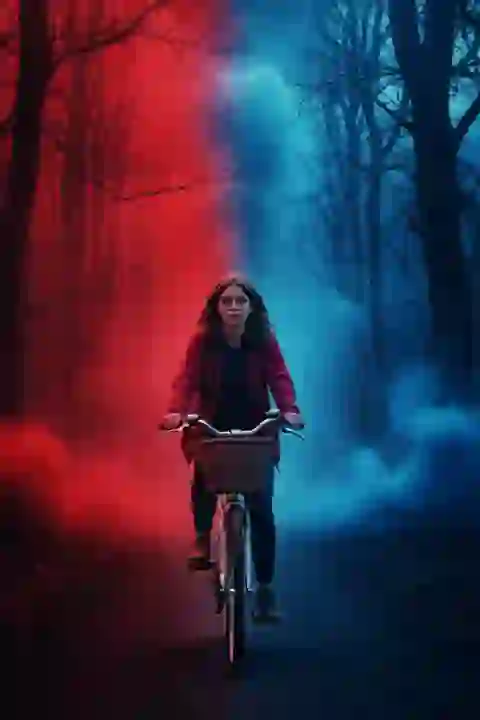 AI-generated image of a girl riding a bicycle through a dark forest with red and blue smoky mists swirling around bare, twisted trees, creating a dramatic Stranger Things-inspired effect.