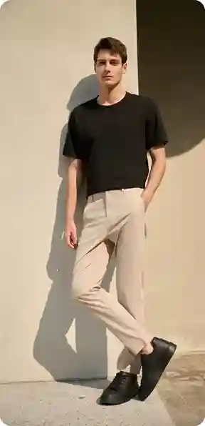 En mand i en sort t-shirt og beige bukser, stående udendørs, model for AI-tøjbytte.