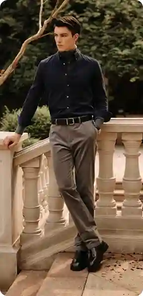 En mand i en mørkeblå skjorte og grå bukser, lænet op ad et rækværk i en have, model for AI-tøjbytte.