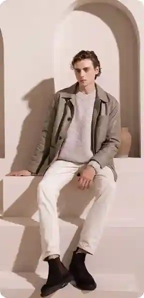 En mand i en grå blazer, lysegrå sweater og hvide bukser, siddende i et minimalistisk rum, model for AI-tøjbytte.