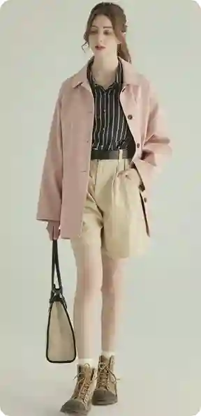 En kvinde i en lyserød jakke, stribet skjorte og beige shorts, holder en beige taske, i brune støvler, model for AI-tøjbytte.