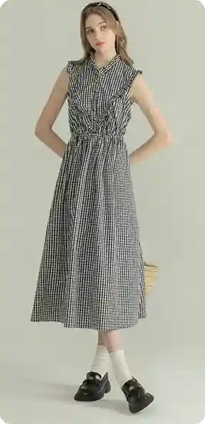 En kvinde i en ærmeløs ternet kjole, stående med en hånd på hoften, i sorte sko og hvide sokker, model for AI-tøjbytte.